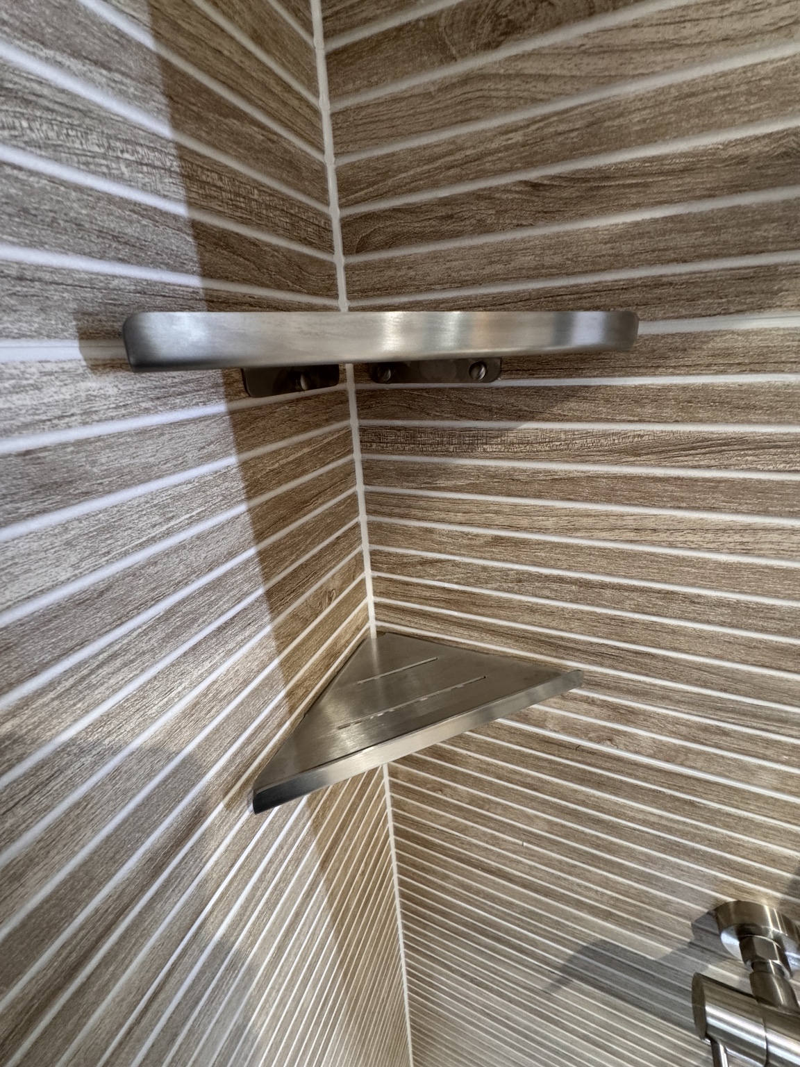 Brushed metal corner shelf detail in a tiled shower
