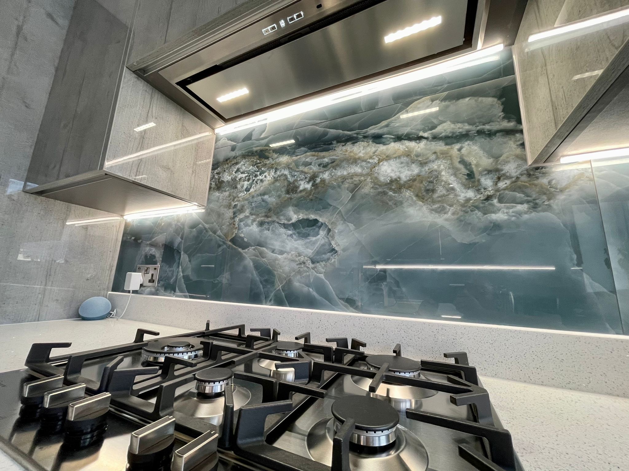 Blue stone-effect splashback and gas hob beneath illuminated cabinets