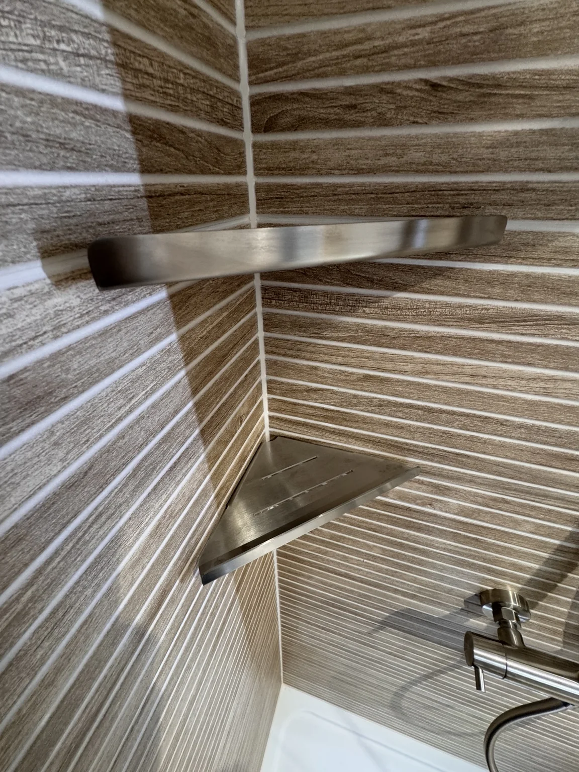 Brushed-metal corner shelves fitted against textured shower tiles