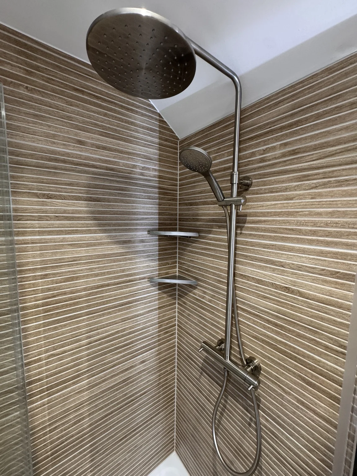 Overhead shower and handset against textured wood-effect tiles