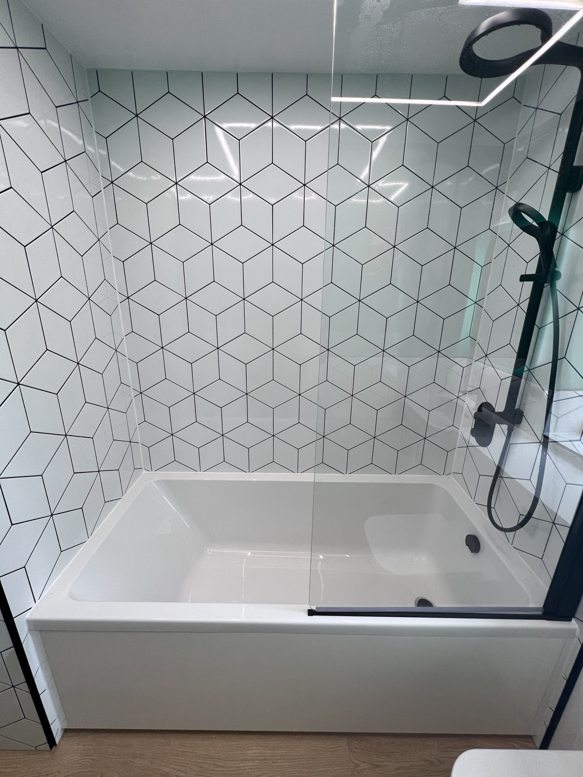 New white bath with black shower screen and geometric tiling